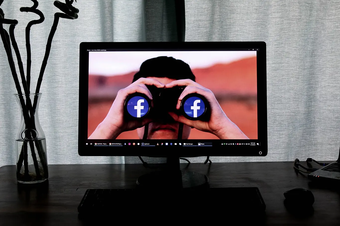 Man looking through binoculars, on a tv, which shows facebook logo