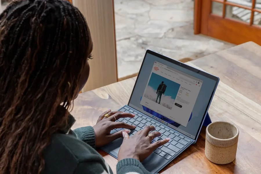 Woman of colour, typing on a laptop, sitting at a wooden table with a mug